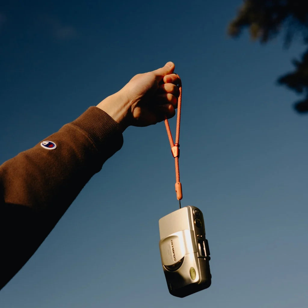 Hand holding a vintage camera with a Mobile Cuff in color Ibis against a clear blue sky